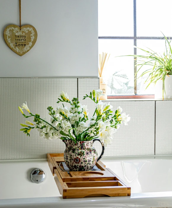 some white flowers are in a pitcher on a bath tub