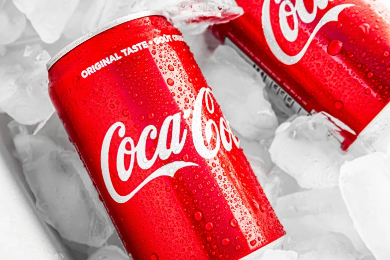 two cans of coca cola sitting on ice