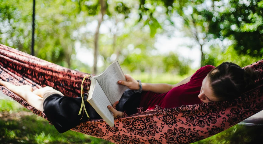 a woman laying in a hammock reading a book