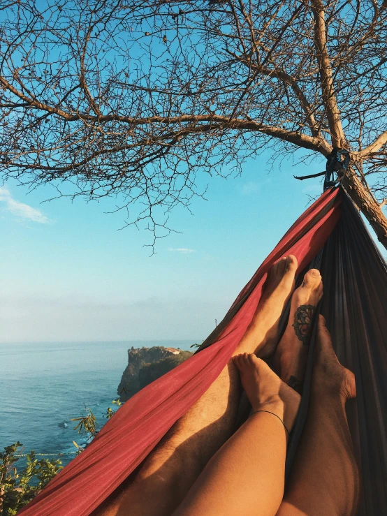 someone's feet resting on a hammock over the ocean