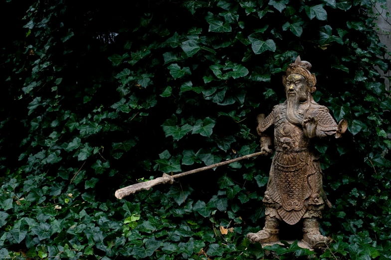 a statue with a baseball bat in front of green plants