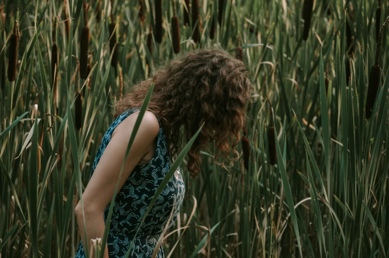 woman standing in tall grass looking at flowers