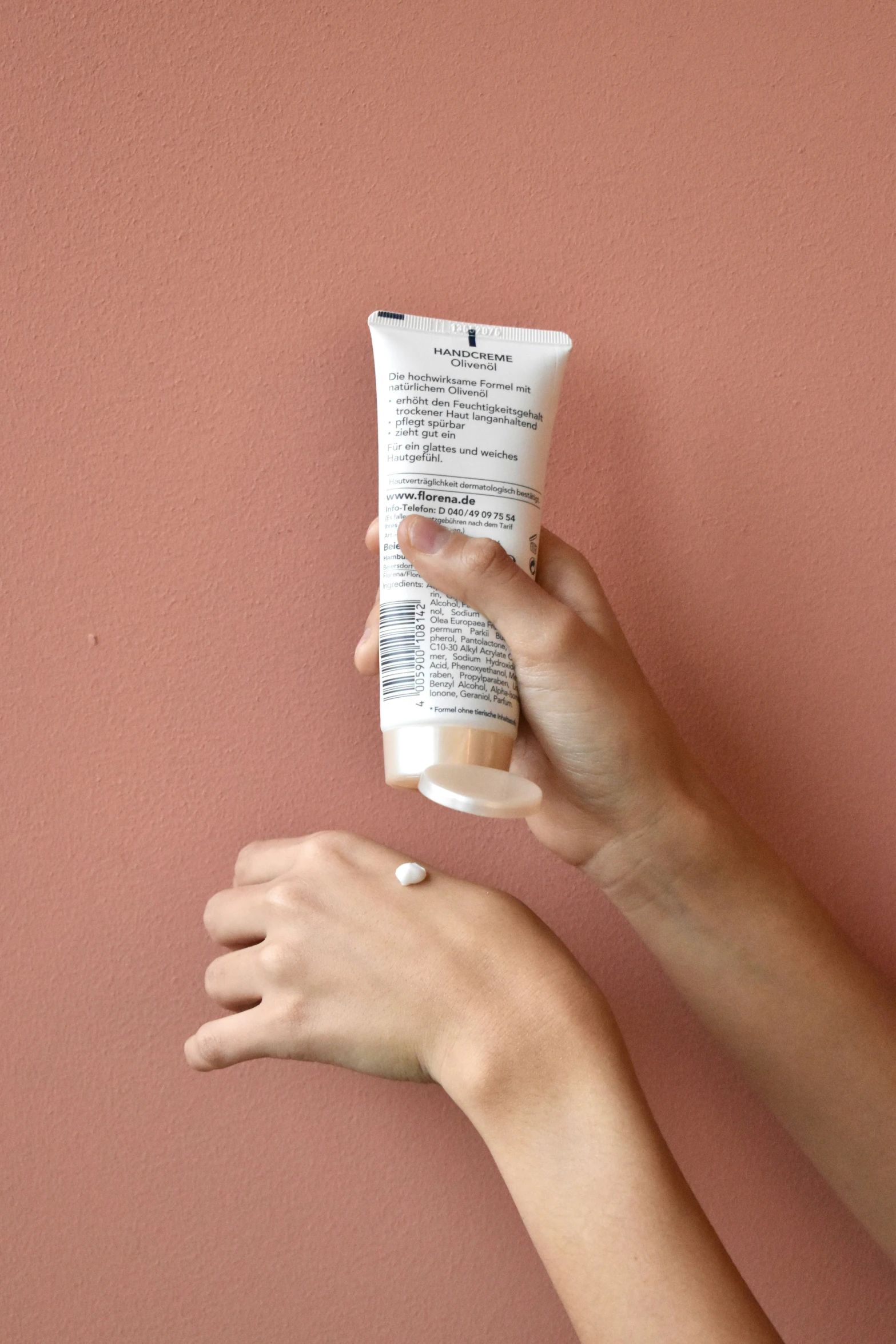 hands holding a tube of cream near a pink wall