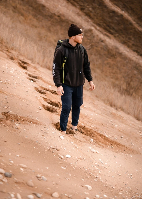 a man walking uphill wearing a black hat