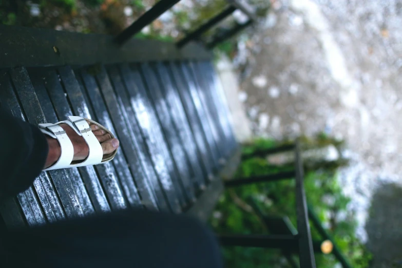 the shoeless feet and foot of a person sitting on a wooden bench