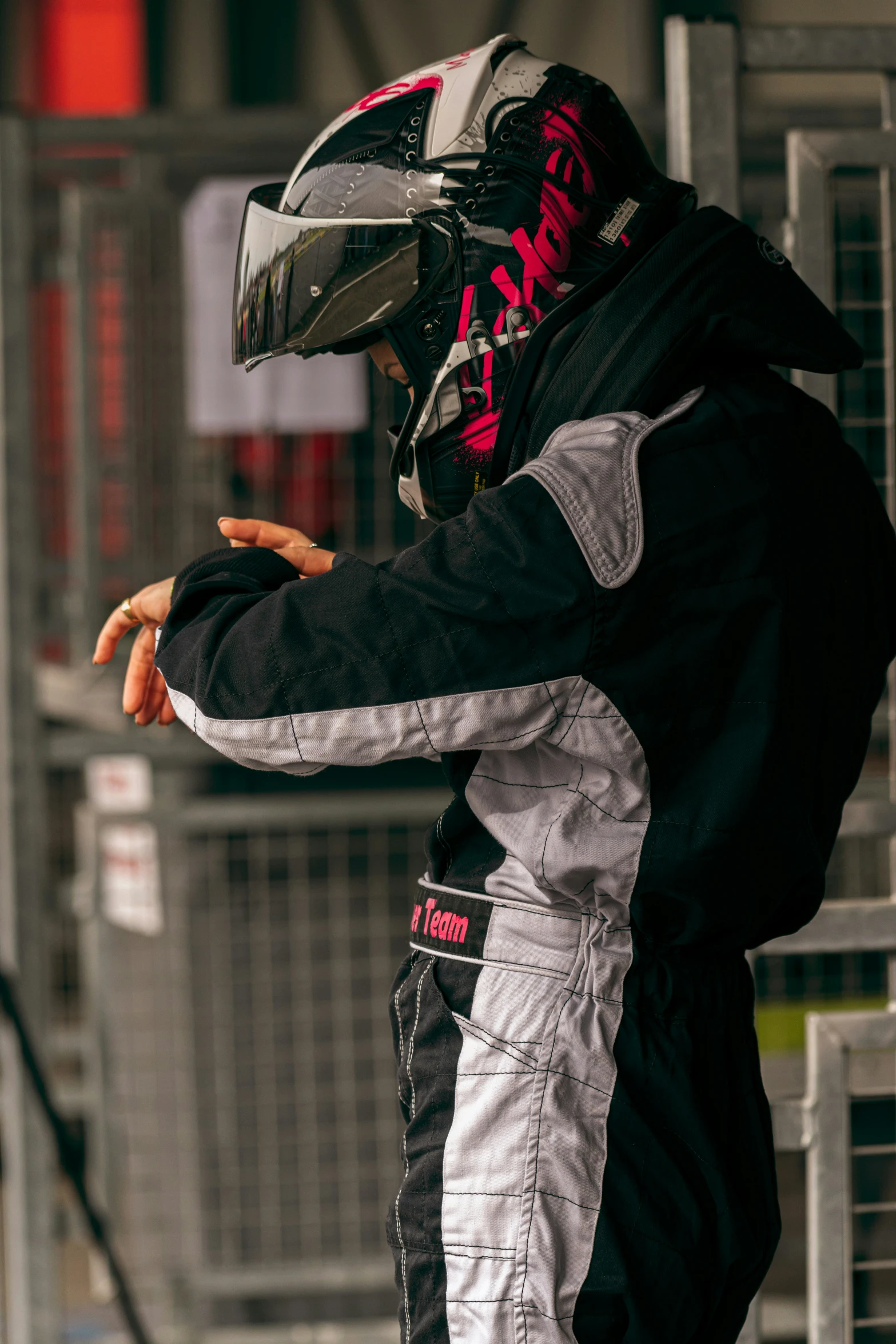 a man wearing a motorcycle outfit and full helmet leaning against a metal fence