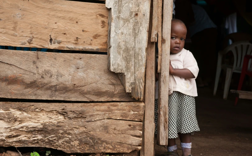 a small boy standing outside of a wooden hut