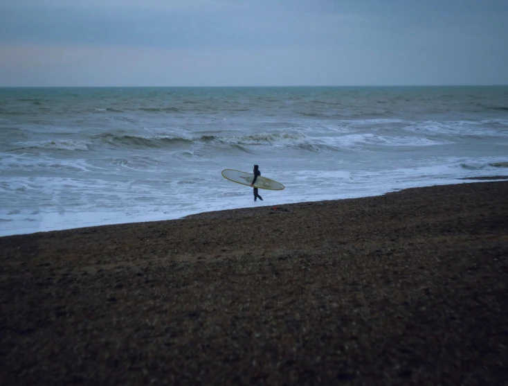 a lone person walks down to the sea with a surfboard