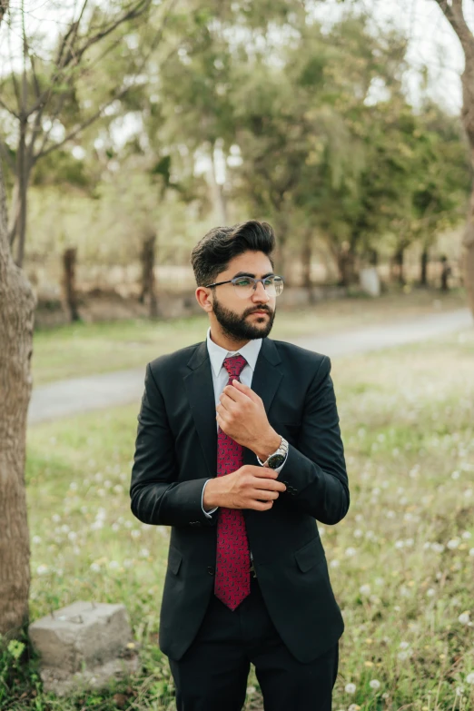 a young man wearing a black suit standing in the woods