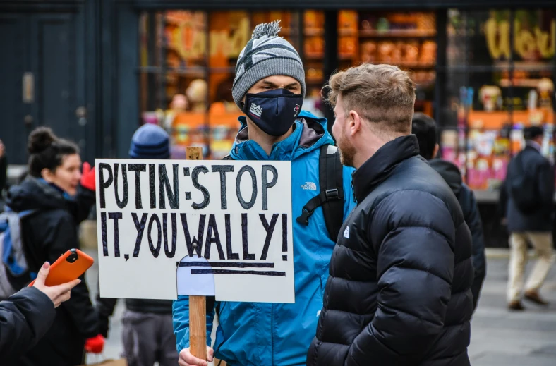 a woman holding a protest sign, with another person wearing a mask