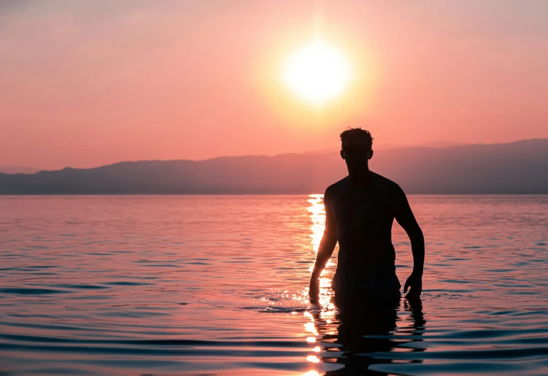 a man standing in water while the sun sets