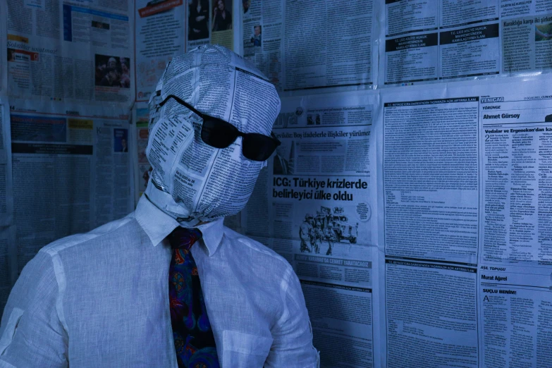 a man in a white shirt, tie and sunglasses, next to a wall with papers on it