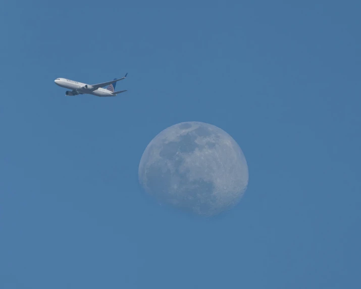 an airplane flies past the moon in a clear sky