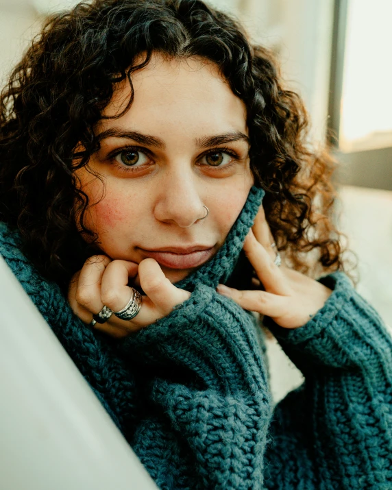 woman wearing blue sweater leaning against window looking at camera