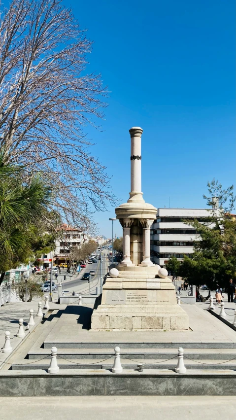 a city monument with people sitting on benches and trees in the background