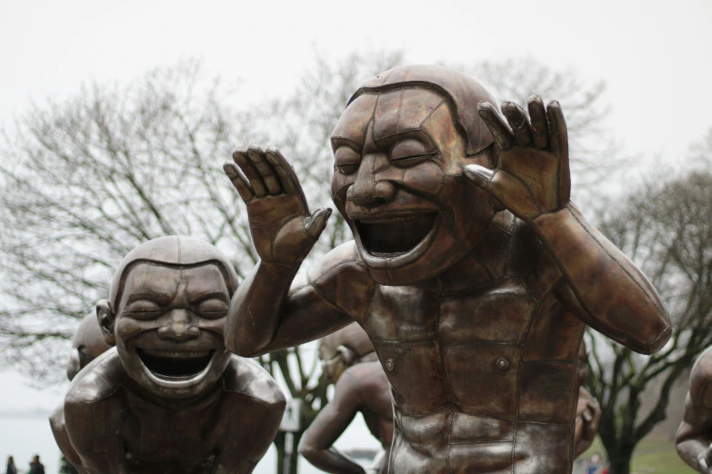 several statues of laughing faces with trees behind them