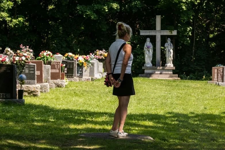 woman with red bouquet standing near headstones at cemetery