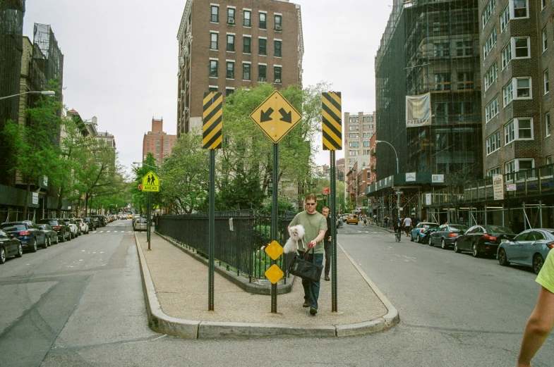 a man is crossing the street in front of a large yellow traffic sign