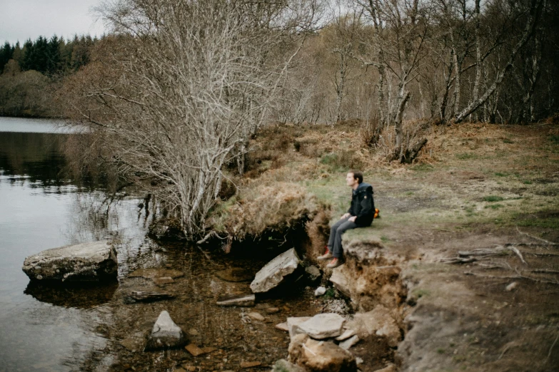 there is a man sitting on the rock near a river