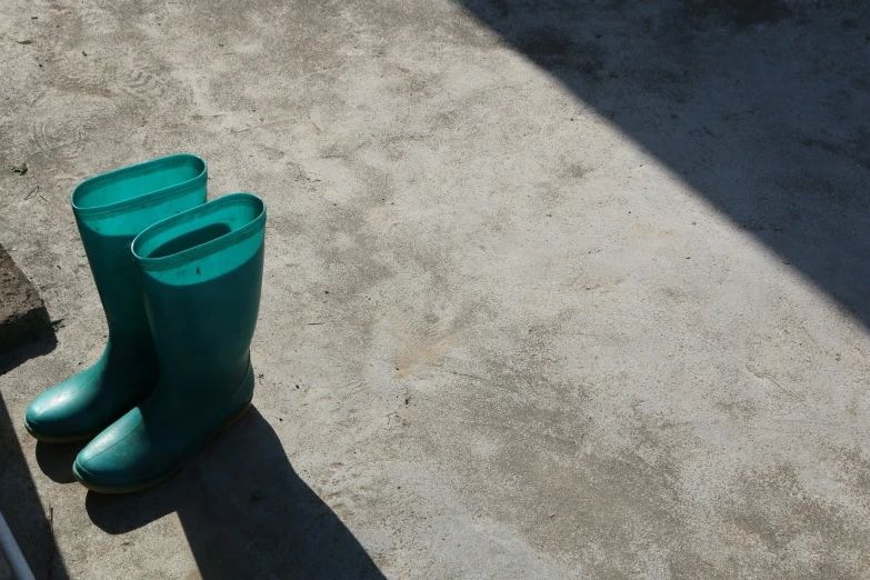 three green boots are leaning against the concrete