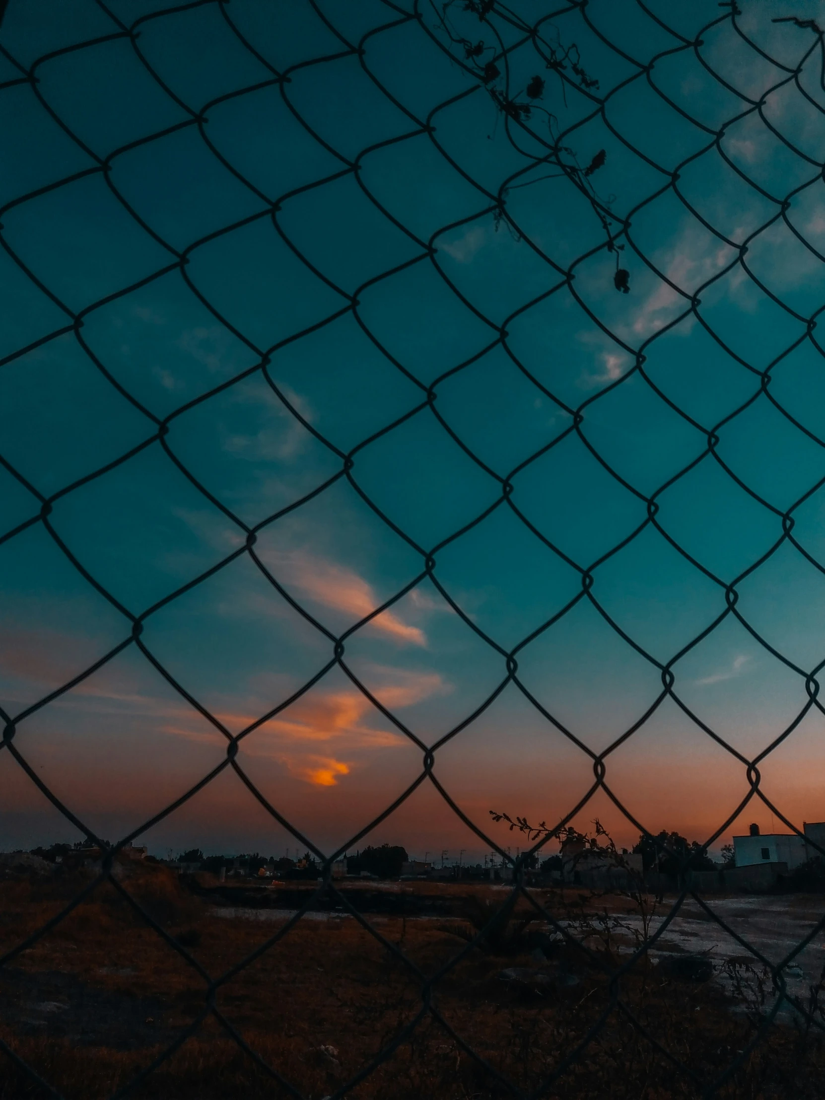 a chain link fence in a field with the sun setting behind it
