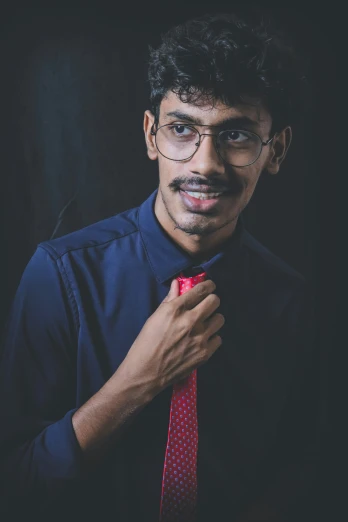 a person is wearing glasses and is tying a red tie