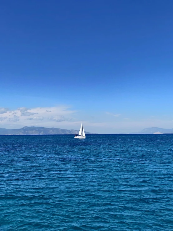 a sailboat on a blue ocean with the background mountains