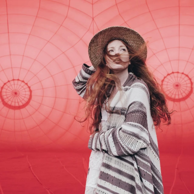 a woman standing in front of a red wall wearing a hat