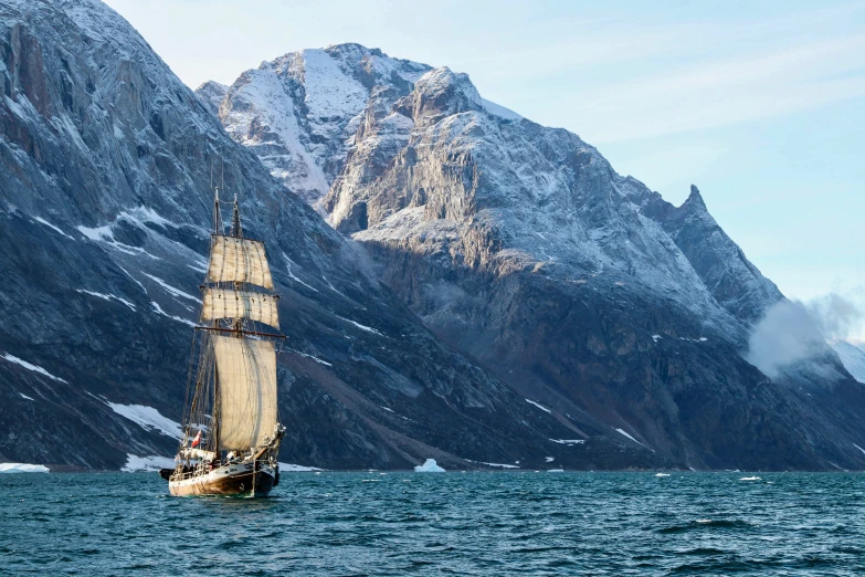 the sailboat is traveling on the waters near snow capped mountains