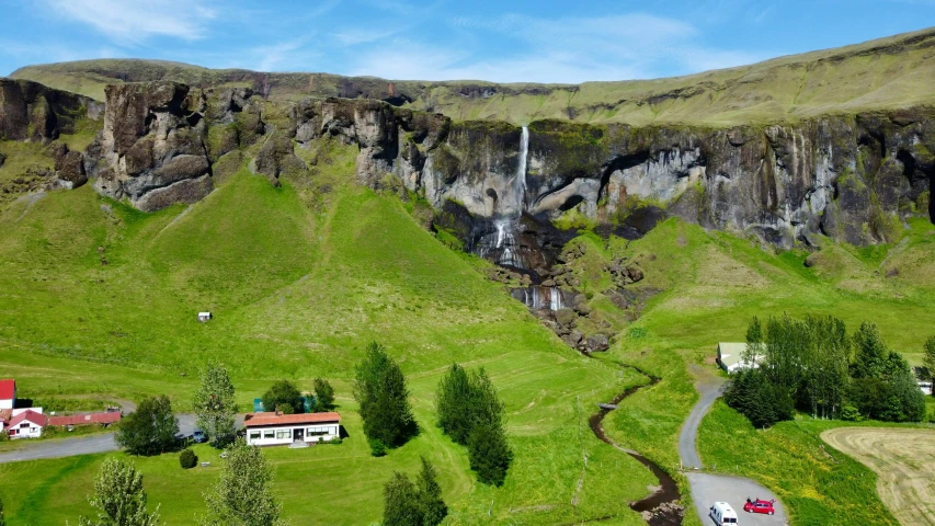 there is a green field and mountains that have a small waterfall