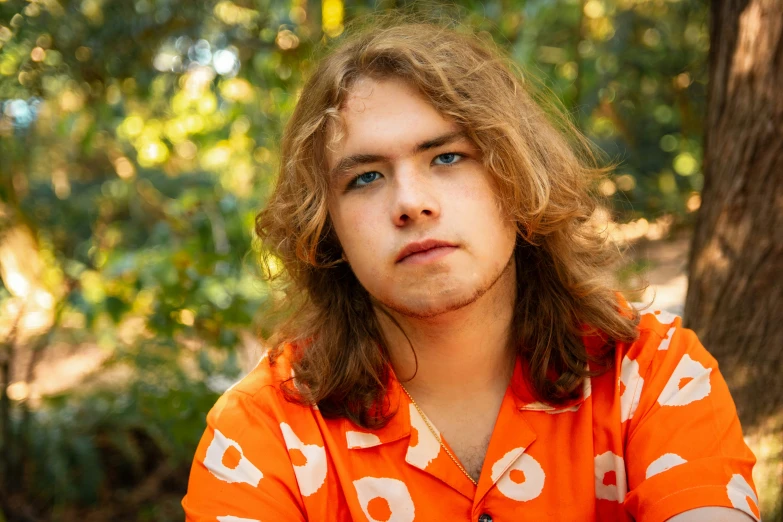 a young man is sitting in the woods with his hair in half