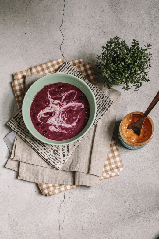 a bowl of beet soup sits on a napkin, next to a spoon