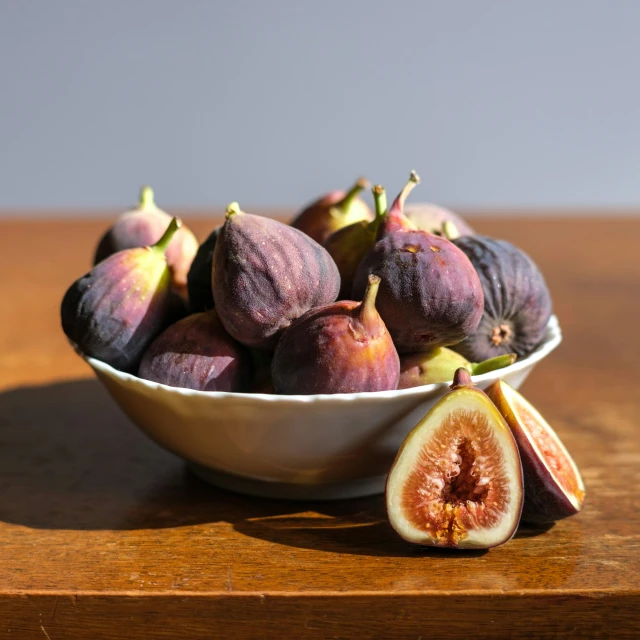 a bowl of figs sitting on top of a wooden table