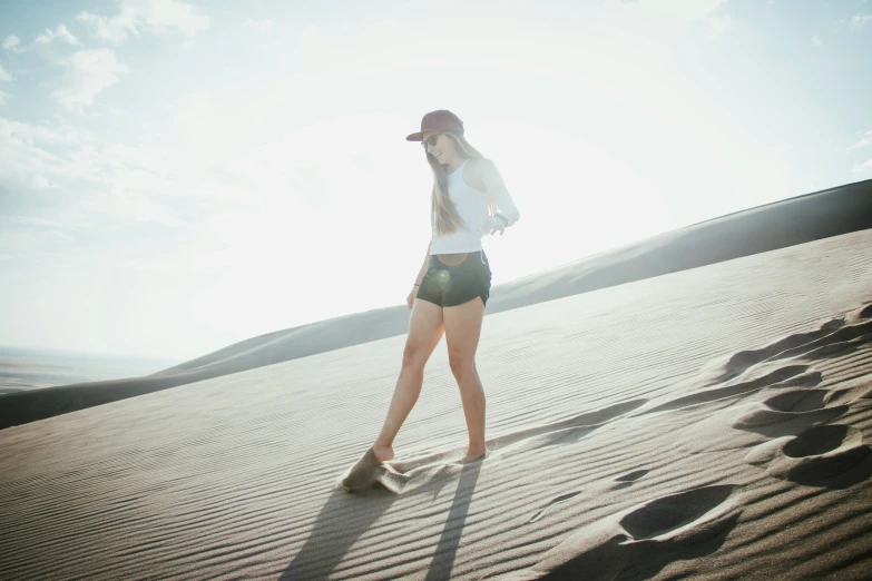 a woman standing in the sand, with her hat on and sunglasses on