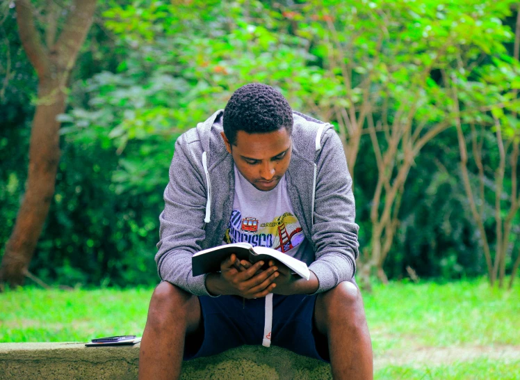 man reading book while sitting on park bench