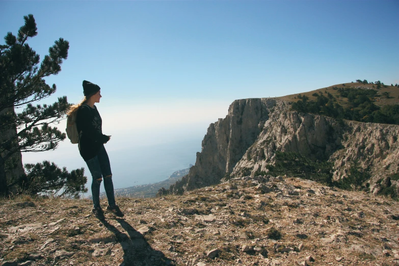 a female hiker in all black stands on a mountain with her back to the camera