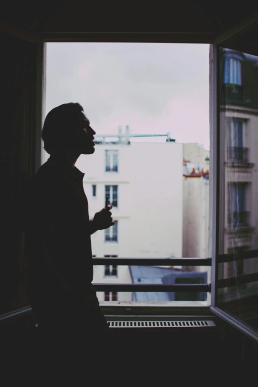 silhouette of a man in the window looking out at buildings