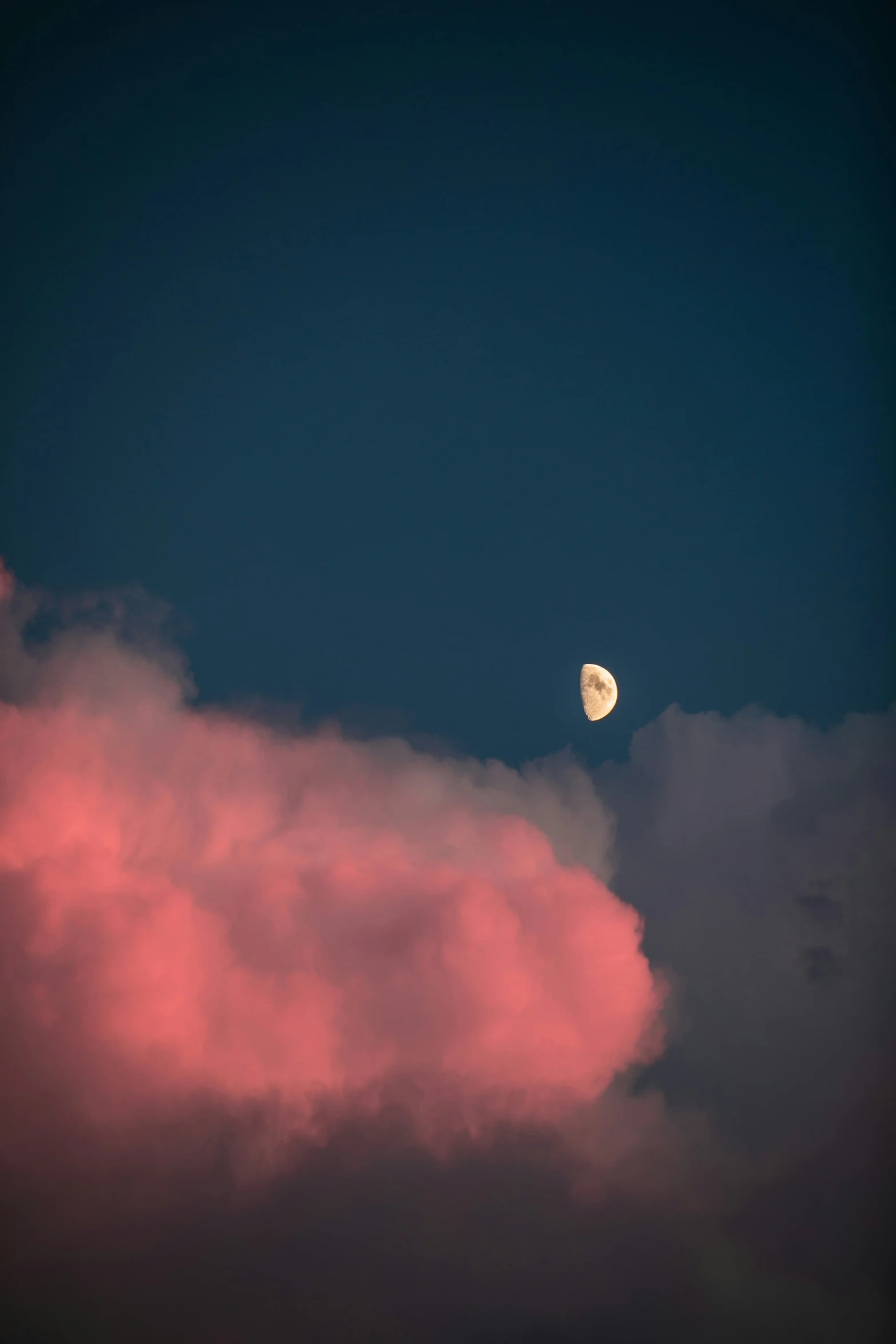 the moon is rising above the clouds with dark blue skies