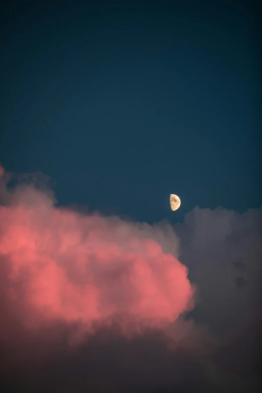 the moon is rising above the clouds with dark blue skies