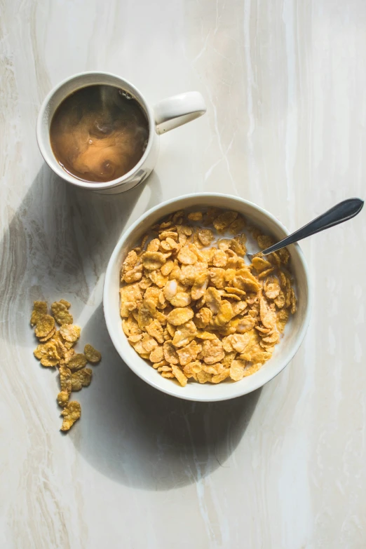 a white bowl containing a granola next to a cup of coffee