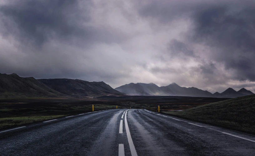 an empty country road leads to mountains in the distance