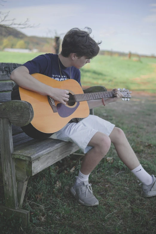 a boy sitting on a bench playing an acoustic guitar