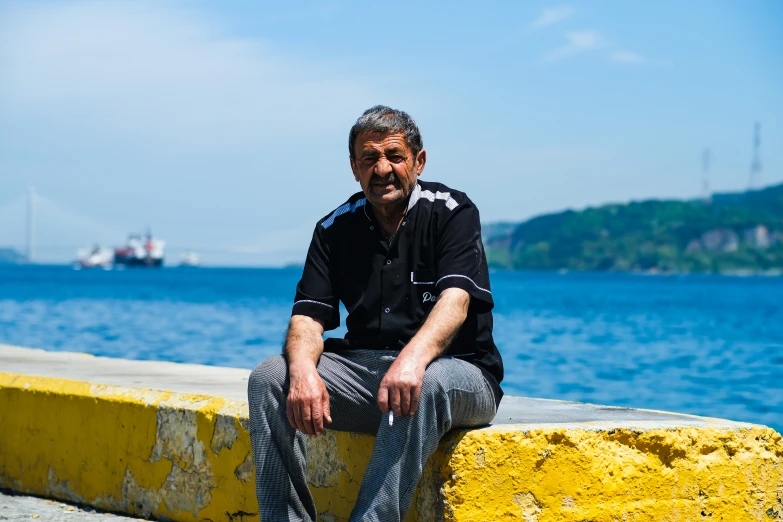 a man sitting on top of a concrete ledge next to water