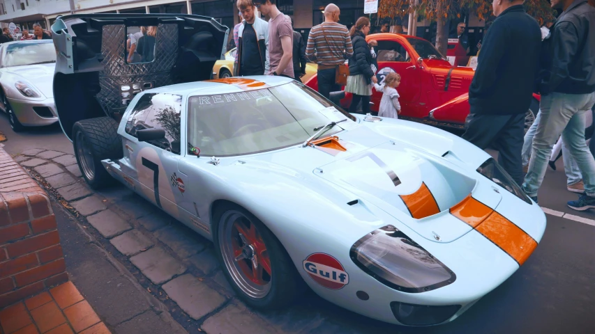 the large white sports car is parked next to people