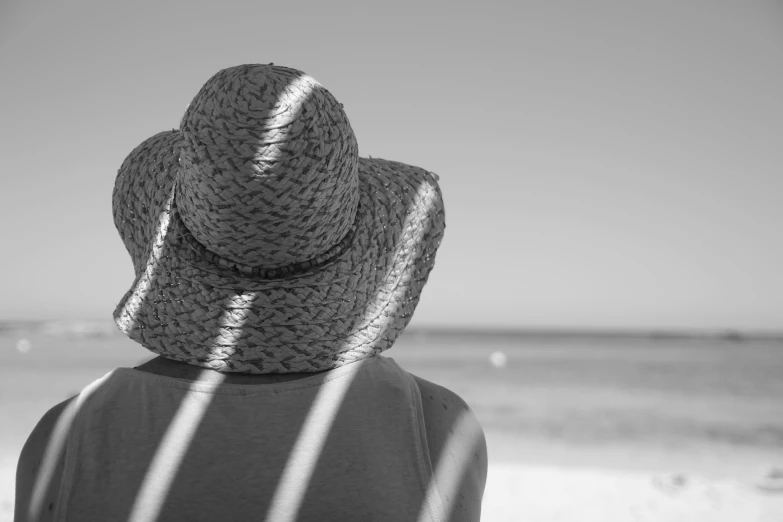 someone's back is covered by a hat as they stand on the beach