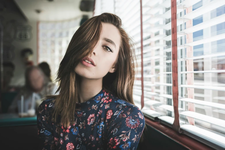 a beautiful woman standing next to a window covered in blinds