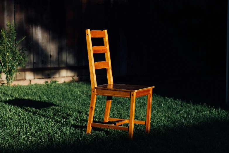 a wooden chair is in the grass near a shed