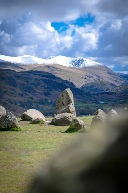 a large rock in a grassy area with some snow capped mountains behind it