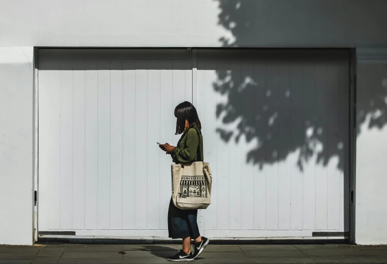 a woman is looking at her phone and holding a tote bag