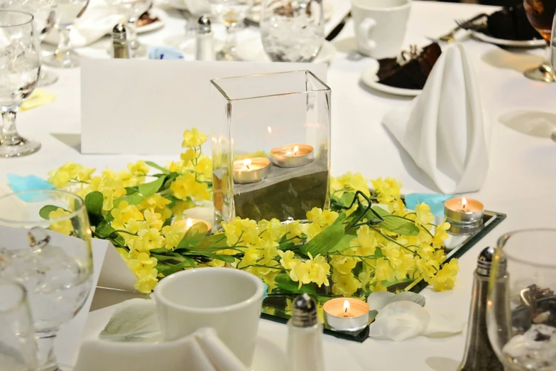 a table with white and yellow dishes and flower centerpieces